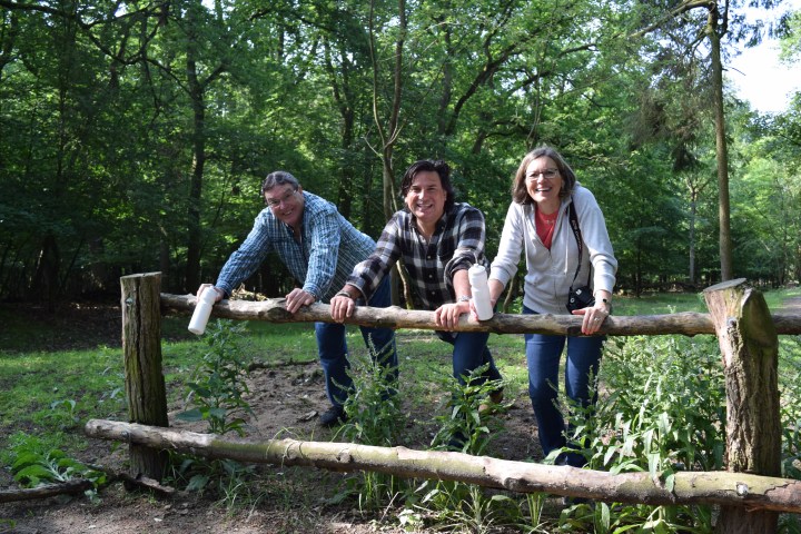 Three people leaning onto a wooden stick in a forest