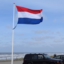 A Dutch flag on a high pole next to the beach