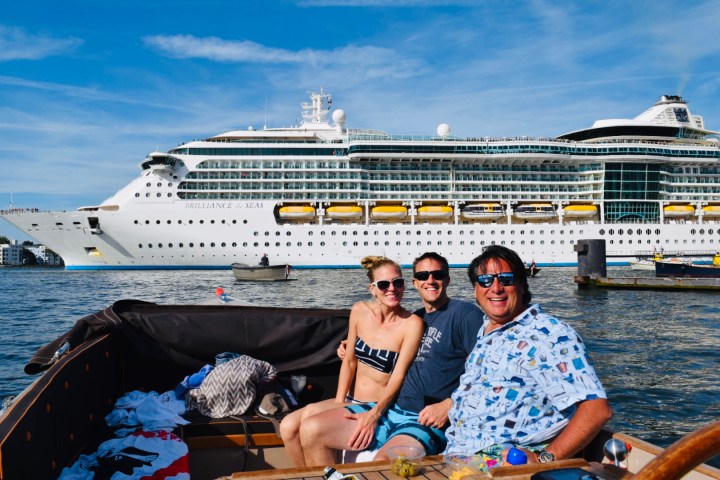 Three people sitting on a boat and a big cruise ship in the background